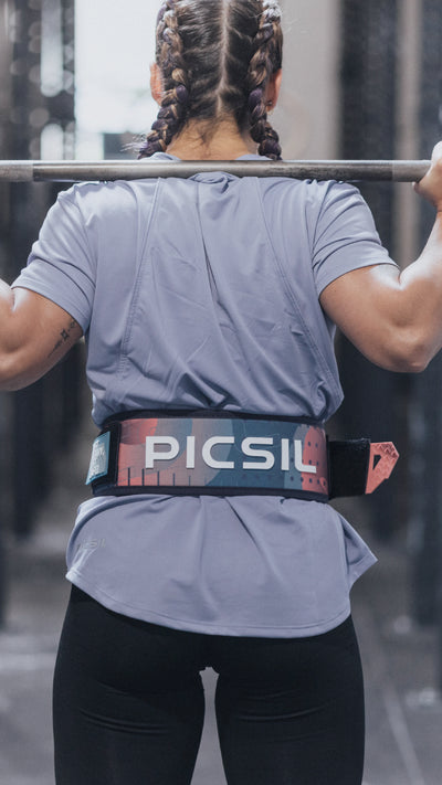 Atleta femenina de espaldas levantando barra en gimnasio, usando cinturón lumbar para entrenamientos de crossfit y halterofilia